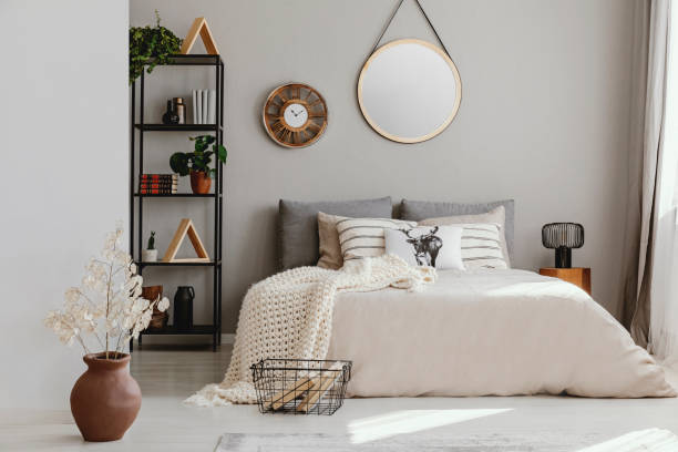 istock Round mirror and clock above bed with pillows in bright bedroom interior with flowers. Real photo 1053814934