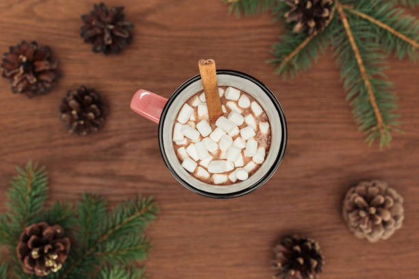 istock top view of cup with hot chocolate, marshmallows, cinnamon stick, coniferous twigs and pine cones on wooden table 1053821012