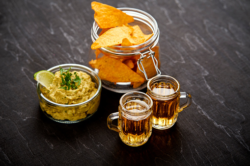 beer and a bowl of guacamole with nachos on an old black wooden table