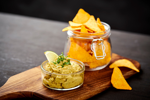 bowl of fresh delicious guacamole and a jar of nachos on an old black wooden table