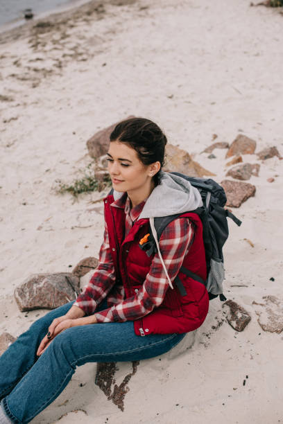 istock pensive woman with backpack resting on rocks on sandy beach 1053828566