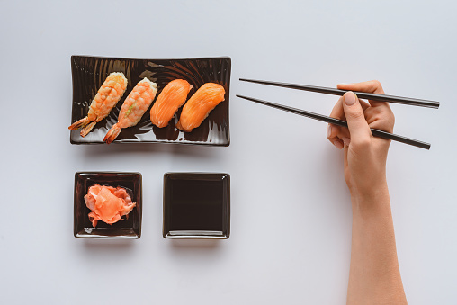 cropped shot of person holding chopsticks and eating delicious sushi isolated on white