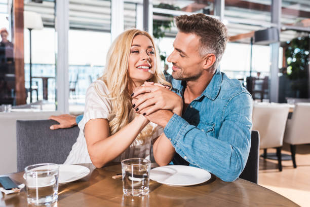 istock cheerful couple holding hands and looking at each other at table in cafe 1053834498