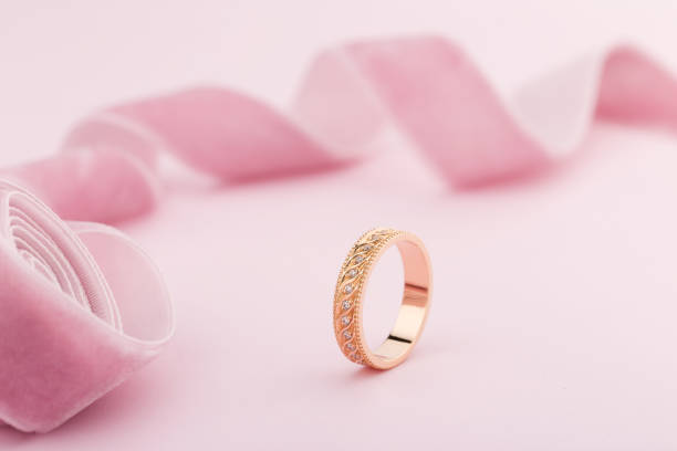 istock Pink gold wedding ring with diamonds and wave pattern on pink background 1053835772