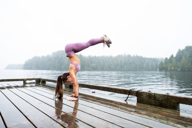 Young girl performs handstand on log on mountain lake, below mountains and forest, Whistler, B.C.