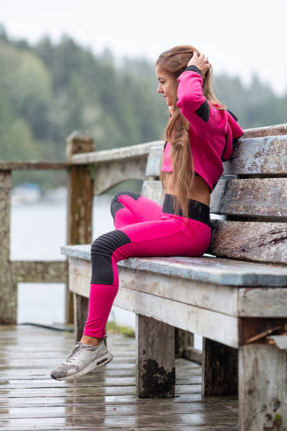 jeune femme qui s’étend et sur banc de repos après des pluies d’entraînement - sweat women wet shirt photos et images de collection