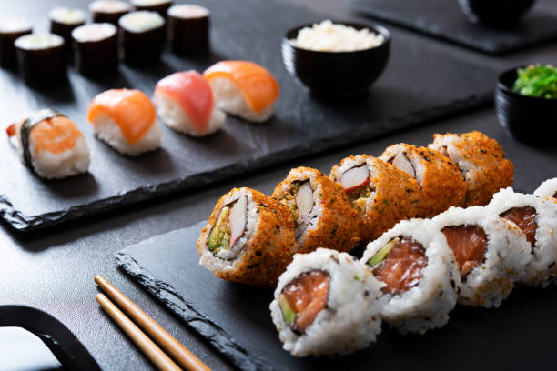 Sushi set at japanese restaurant Japanese sushi food served on blackboard plate with bowl of rice and seaweed. Sushi roll with prawn, avocado, cream cheese, sesame. Uramaki, hosomaki rolls and nigiri on black table with chopstick. japanese cuisine food rolled up japanese culture stock pictures, royalty-free photos & images