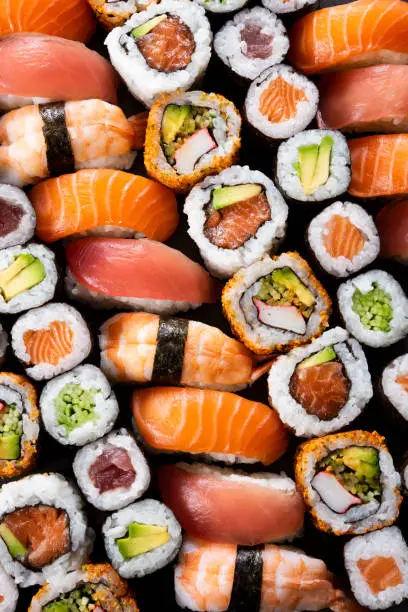 Top view of variety of sushi food. High angle view of nigiri, maki, hosomaki, uramaki and roll with tuna, salmon, avocado and shrimp in a row. Traditional japanese food with raw fish and rice.