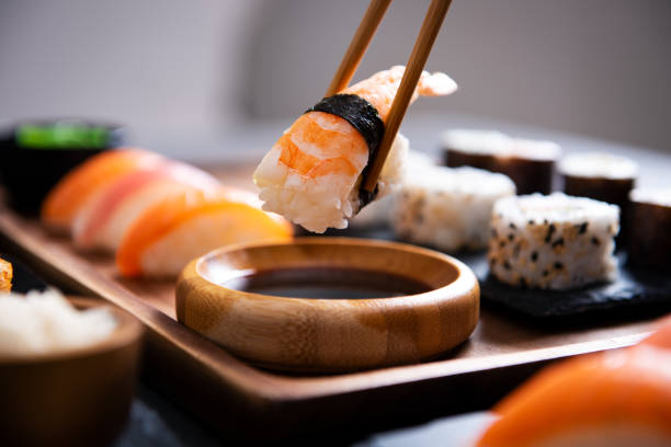 Chopstick with nigiri sushi piece Closeup hand holding bamboo chopsticks with nigiri shrimp while soaking it in soy sauce. Detail of sushi set on wooden tray at restaurant while hand dip nigiri in soy sauce. Japanese cuisine concept. sushi stock pictures, royalty-free photos & images