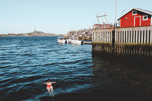 Woman swimming in cold ocean near fishing village on Lofoten Islands