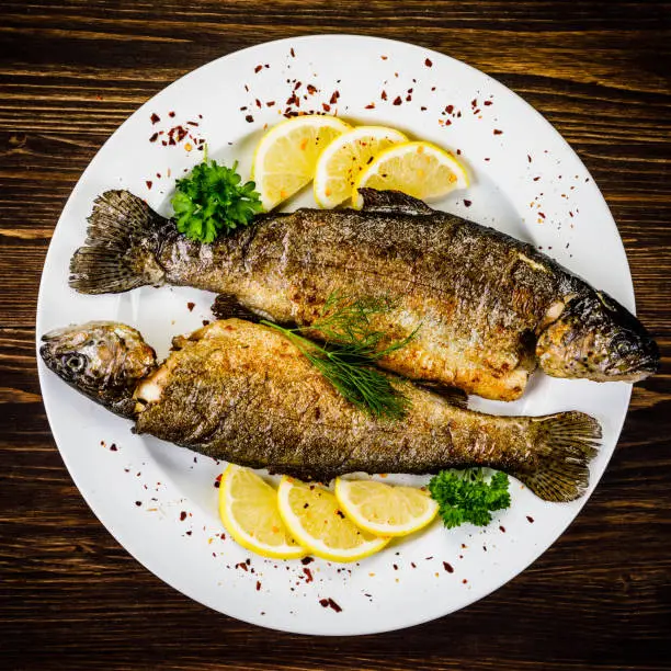 Fried fish on white plate on wooden background