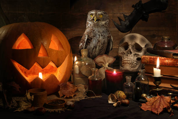 Scary still life with skull, pumpkin, old books, maple leaves, vintage bottles, candles and a Eurasian scops owl sitting on a witch table. Halloween or esoteric concept.