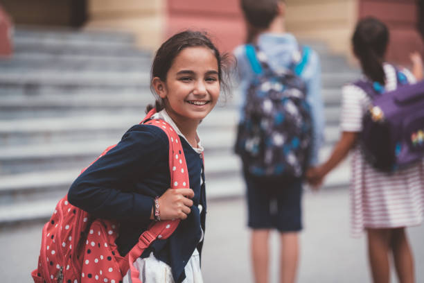Cute schoolgirl smiling before entering the school building