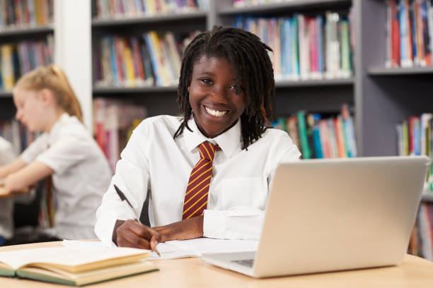портрет студентки средней школы в униформе, работающей за ноутбуком в библиотеке - uniform стоковые фото и изображения