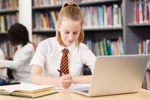 istock Female High School Student Wearing Uniform Working At Laptop In Library 1053901438
