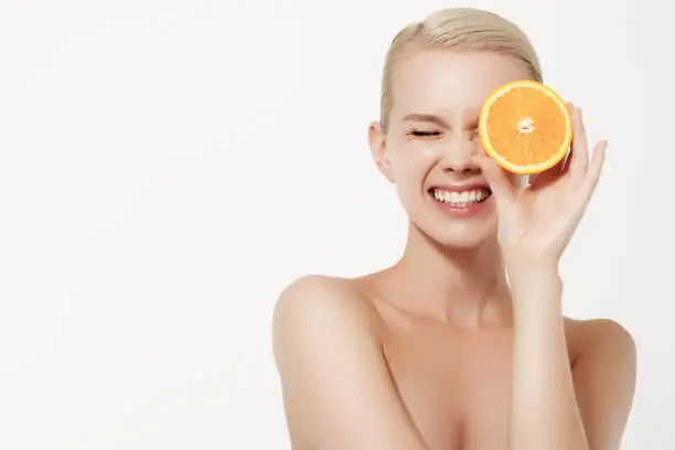 Smiling girl with fresh fruits. Beauty model takes juicy oranges. Joyful girl with freckles. The concept of a healthy diet. Professional make up. Orange slice
