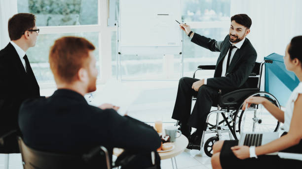 istock Man in Wheelchair Shows Pointer to White Board. 1053909410