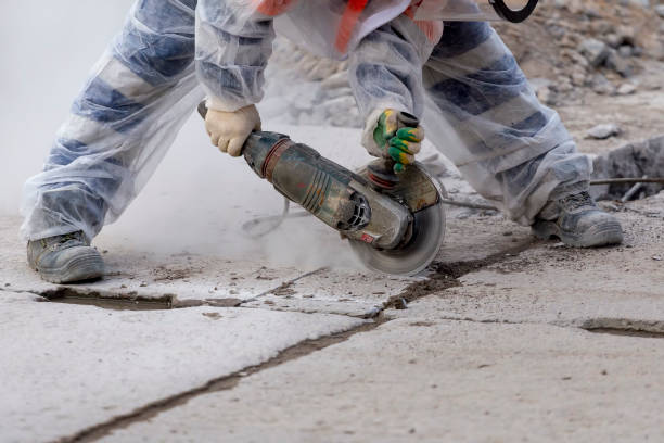 worker catching and using electric cutting machine tool to cut concrete floor with dirty dust spreading in air, stock photo