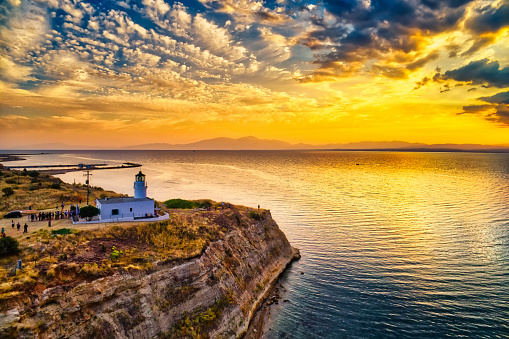 Beautiful view of the seascape in Greece during a sunset. The sun is going down and the sky is becoming orange. The sea is calm and surrounded by high steep cliffs.