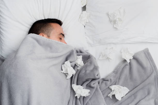 ill man in bed surrounded by used tissues high angle view of an ill young caucasian man in bed, covered with a light gray blanket, surrounded by used tissues handkerchief photos stock pictures, royalty-free photos & images