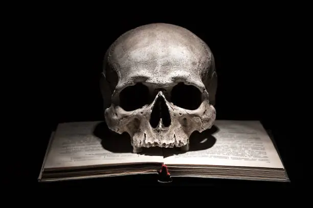 Photo of Human skull on old open book on black background. Dramatic concept.