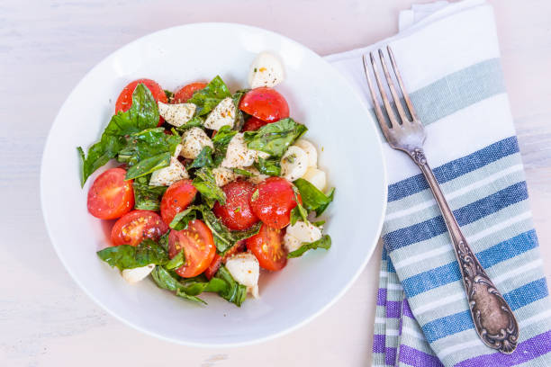 istock Delicious caprese salad with cherry tomatoes and mozzarella cheese with basil on a plate with a napkin and a fork on a bright table 1053932916