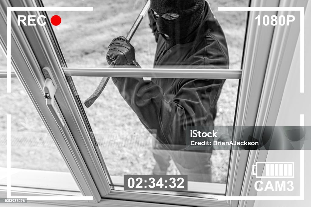 CCTV view of burglar breaking in to home through window CCTV view of burglar breaking in to home through window with crowbar Thief Stock Photo