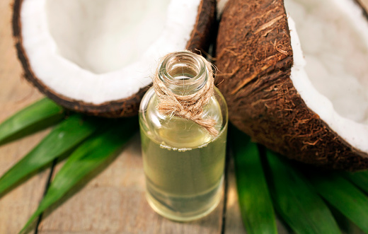 Coconut with green palm leaves and melted coconut oil in a bottle on wooden background.