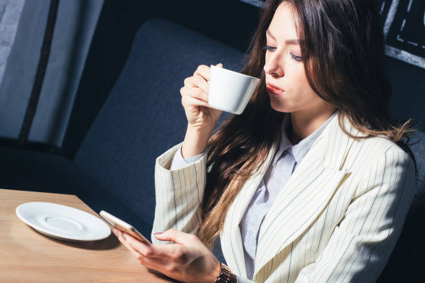 istock Modern girl sitting at the table drinking coffee and using a mobile phone. 1053958338