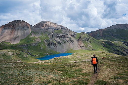 Teenage female hiker walks on a trail through tundra in a stunning  landscape toward alpine Ice Lake nestled in the mountains  in the Upper Basin at 12,600 feet elevation on a summer day, San Juan National Forest,  Silverton, Colorado, USA