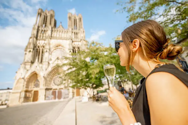 Young woman enjoying champagne standing in front of the cathedral in Reims city, capital of Champagne wine region, France