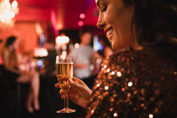 Over Shoulder Shot of Woman Holding a Glass of Champagne Over shoulder close-up shot of a female smiling while in a bar holding a glass of champagne. english spoken stock pictures, royalty-free photos & images