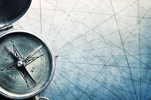 A close up of a compass as it rests on the converging navigational lines of an old map.