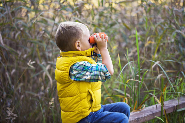 istock Little boy with binoculars sitting on a wooden fence 1054052524