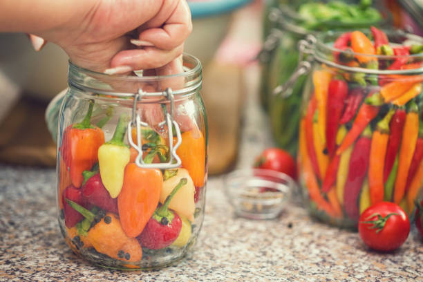 Young women preserving fresh organic chili peppers in jars at home