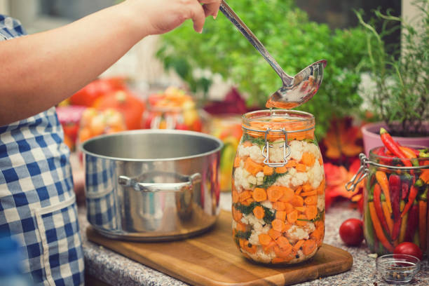 Young women preserving fresh organic cauliflower,carrots and garlic in jars at home