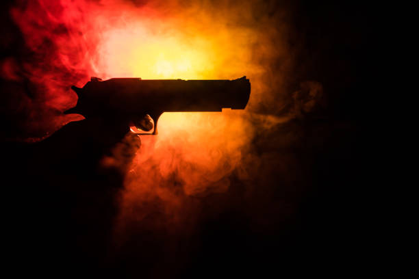 istock Male hand holding gun on black background with smoke ( yellow orange red white ) colored back lights 1054084514