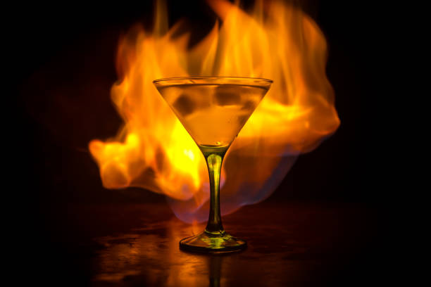 martini in feuer-konzept. glas des berühmten cocktail martini brennen bei feuer im dunkel getönten nebligen hintergrund. - martini brand vermouth stock-fotos und bilder