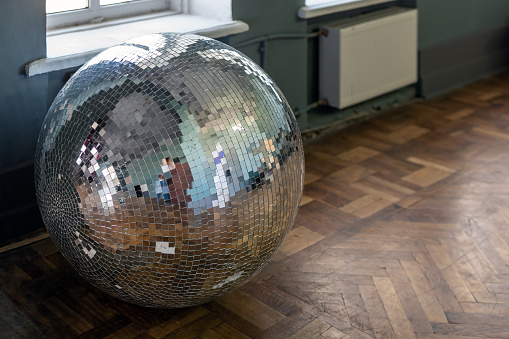 Removed old disco ball on hardwood wooden floor. Needless nightclub accessory from past. End of party concept.