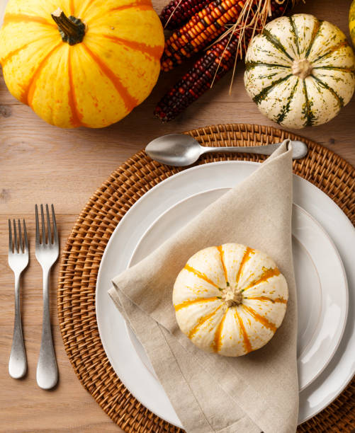 istock Festive Fall Thanksgiving table setting place setting home decorations with china plates dishes, silverware, linen cloth napkin, placemat, natural miniature pumpkins and ornamental squash on rustic wooden tabletop. holiday entertaining dinner parties. 1054102338