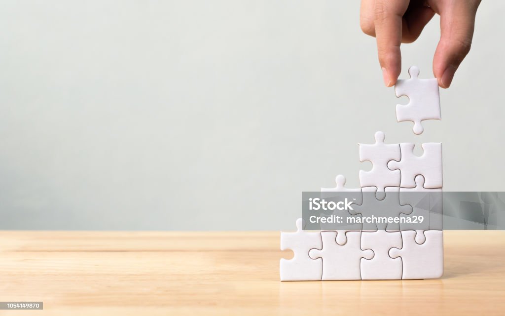 Hand arranging jigsaw puzzle stacking as step stair on wooden table. Business concept for growth success process Building - Activity Stock Photo