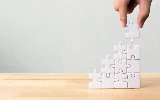 Photo of Hand arranging jigsaw puzzle stacking as step stair on wooden table. Business concept for growth success process