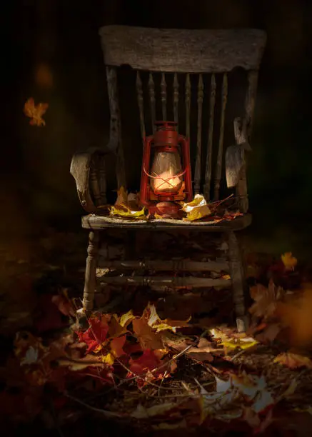Garden scene. Fall leaves, rusty rustic oil lamp, lantern on vintage wooden chair. Dark autumn day in garden, nightlight.