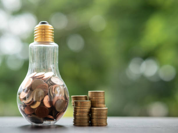 istock Energy saving. stacks of coins in light bulb and tree nature background. Saving, accounting and financial concept. 1054171800