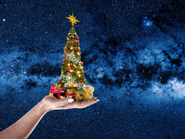 istock Hand holding Christmas tree with gift boxes over stars of galaxy 1054184182