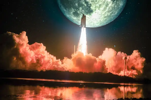 Photo of Lighting up the night sky, as well as the water nearby, spacship blazes into the moon mission. Huge moon is on the night sky surrounding by galaxy. Elements of this image furnished by NASA.