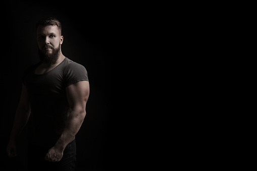 Bodybuilder portrait. Muscular man in a tight t-shirt. Dramatic portrait in unsaturated colors.