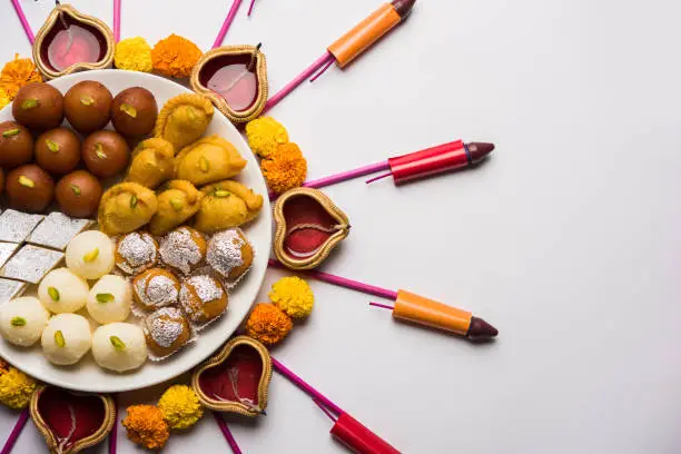 Rangoli or design made using Diya/oil lamp, flowers and sweets likeGulab Jamun, Rasgulla, kaju katli, morichoor / Bundi Laddu, Gujiya or Karanji for diwali celebration