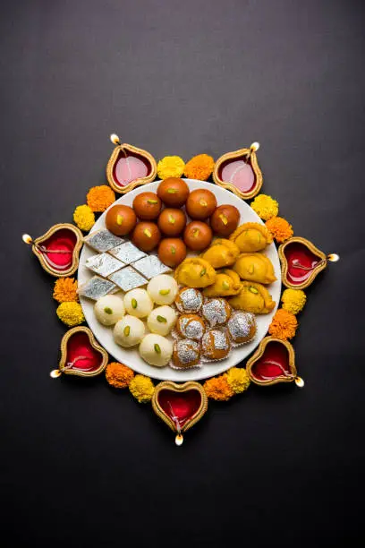 Diwali Rangoli made using Diya/oil lamp, flowers and plate full of Gulab Jamun, Rasgulla, kaju katli, morichoor / Bundi Laddu, Gujiya or Karanji