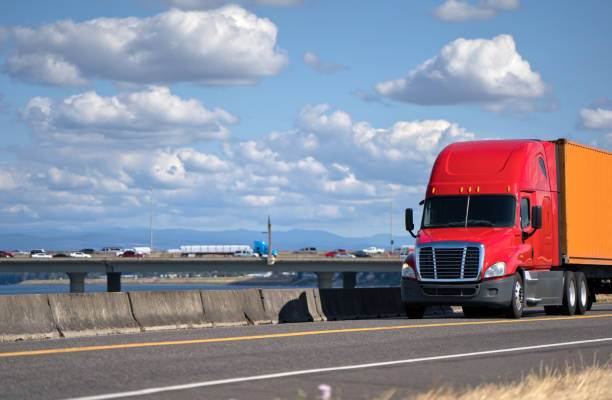 istock Red big rig semi truck transporting container on the road with river and bridge view 1054227696